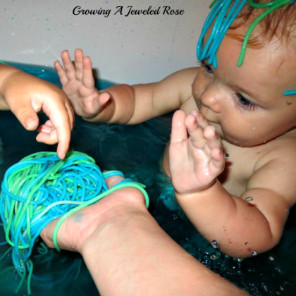 ocean sensory bath - image showing toddler having a bath and playing with blue and green pasta noodles