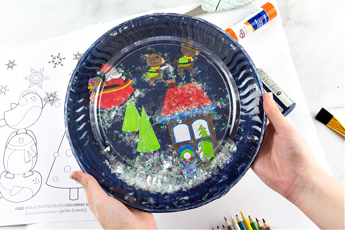 easy paper plate snow globe craft finished with coloring pages in the background from Kids Activities Blog